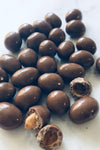 Chocolate peanuts on a white background. 2 of them are broken to show underneath the chocolate coating.