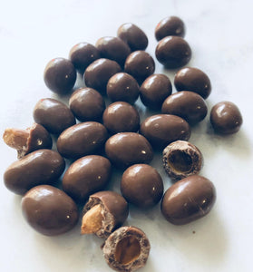 Chocolate peanuts on a white background. 2 of them are broken to show underneath the chocolate coating.