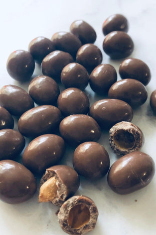 Chocolate peanuts on a white background. 2 of them are broken to show underneath the chocolate coating.