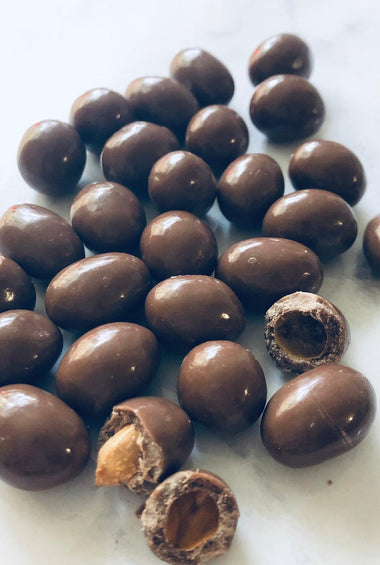 Chocolate peanuts on a white background. 2 of them are broken to show underneath the chocolate coating.