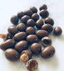 Chocolate peanuts on a white background. 2 of them are broken to show underneath the chocolate coating.