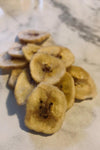 Dried banana slices; banana chips on a white marble table.