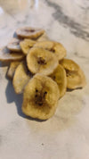 Dried banana slices; banana chips on a white marble table.