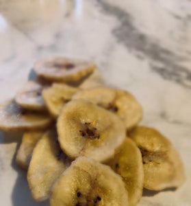 Dried banana slices; banana chips on a white marble table.
