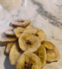 Dried banana slices; banana chips on a white marble table.