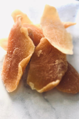 4 chunks of orange preserved mango on a white marble  bench-top.
