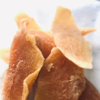4 chunks of orange preserved mango on a white marble  bench-top.