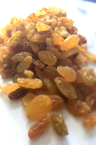 Bright yellow and brown sultanas that sparkle in the light. A large handful takes up most of the image. 