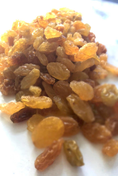 Bright yellow and brown sultanas that sparkle in the light. A large handful takes up most of the image. 