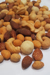 A pile of numerous types of nuts cover most of the image. A white paper background is behind them.