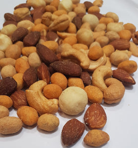 A pile of numerous types of nuts cover most of the image. A white paper background is behind them.