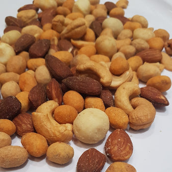 A pile of numerous types of nuts cover most of the image. A white paper background is behind them.