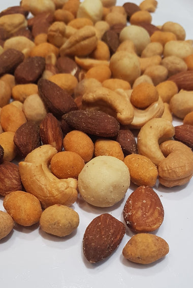A pile of numerous types of nuts cover most of the image. A white paper background is behind them.