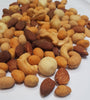 A pile of numerous types of nuts cover most of the image. A white paper background is behind them.